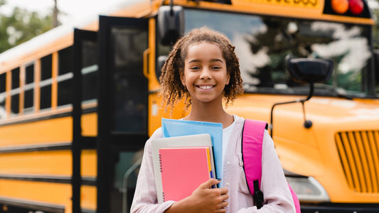 Young African American girl in front of a school bus